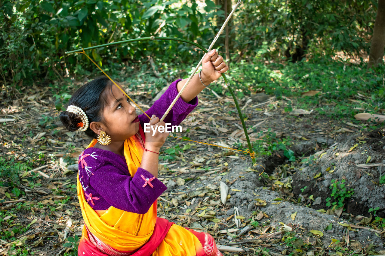 An indigenous indian teenage girl is practicing alone archery in the jungle with a bow and arrow. 