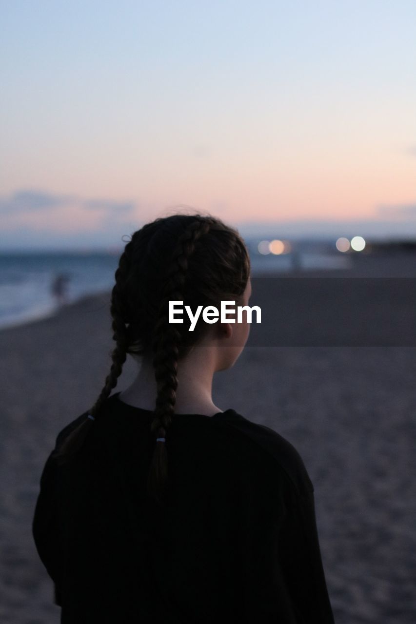 Rear view of teenage girl with braided hair standing on beach against clear sky