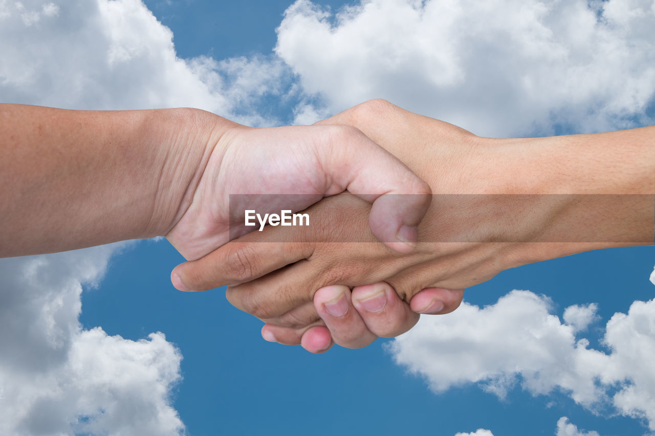 Cropped image of people shaking hands against cloudy sky