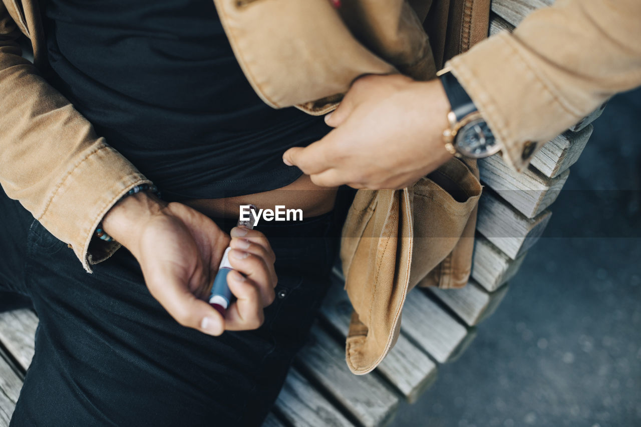 Midsection of man injecting insulin while sitting on bench