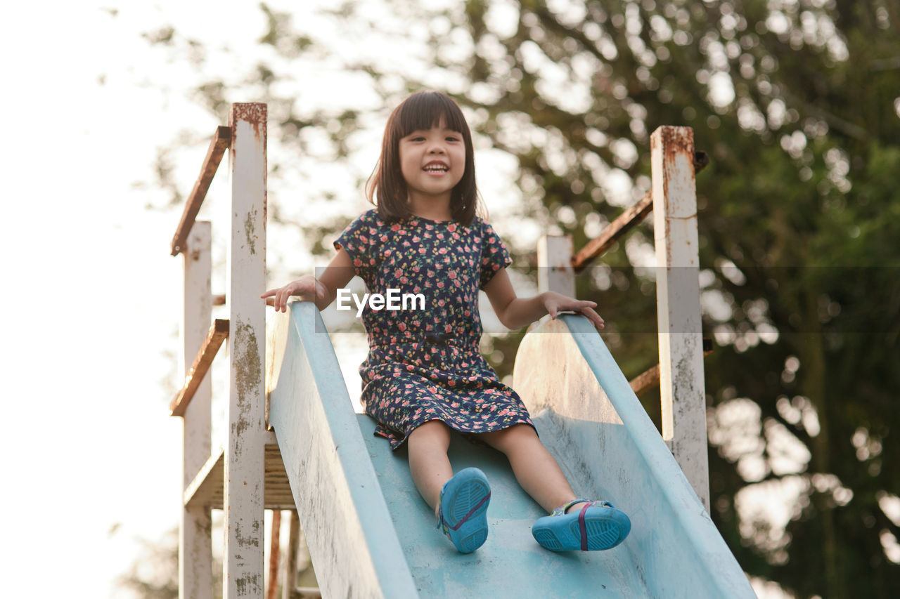 Portrait of girl sliding down on slide in park