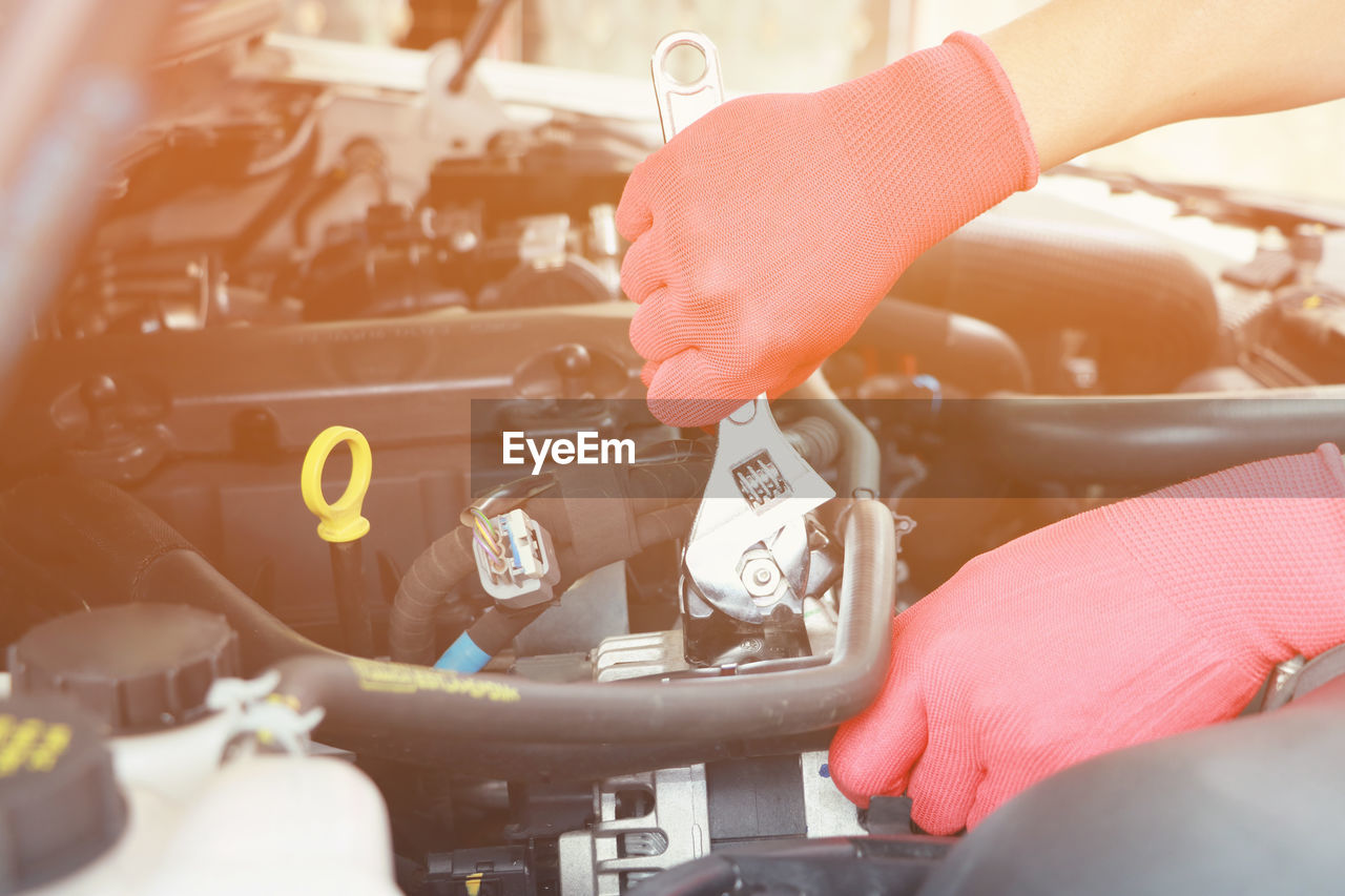 Cropped hands of mechanic holding wrench and repairing car engine