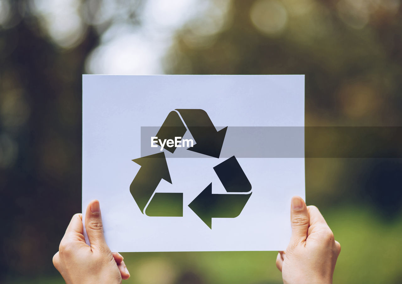 Cropped hands of person holding paper with recycling symbol