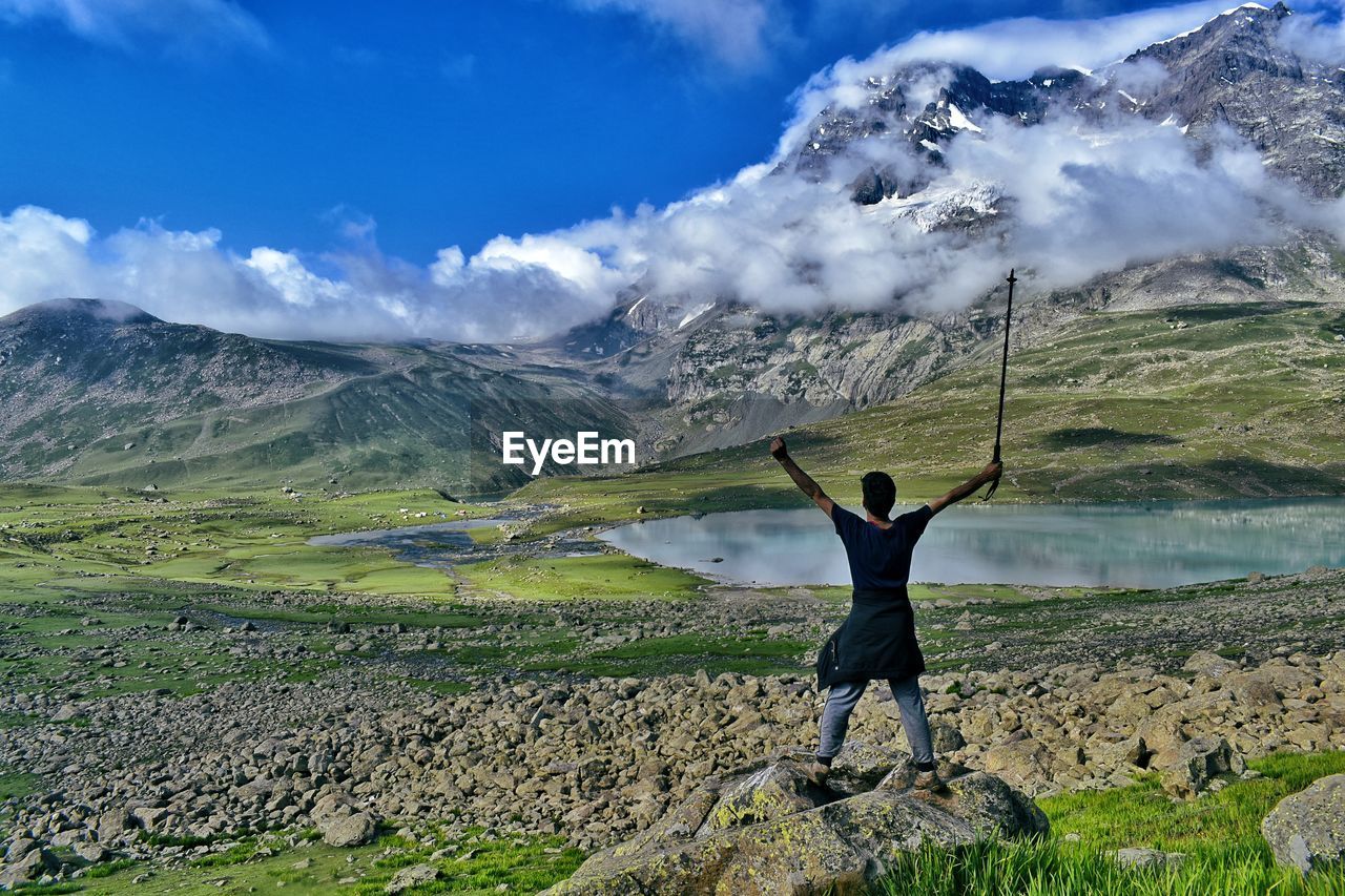 Rear view of man with arms raised standing on rock against mountain