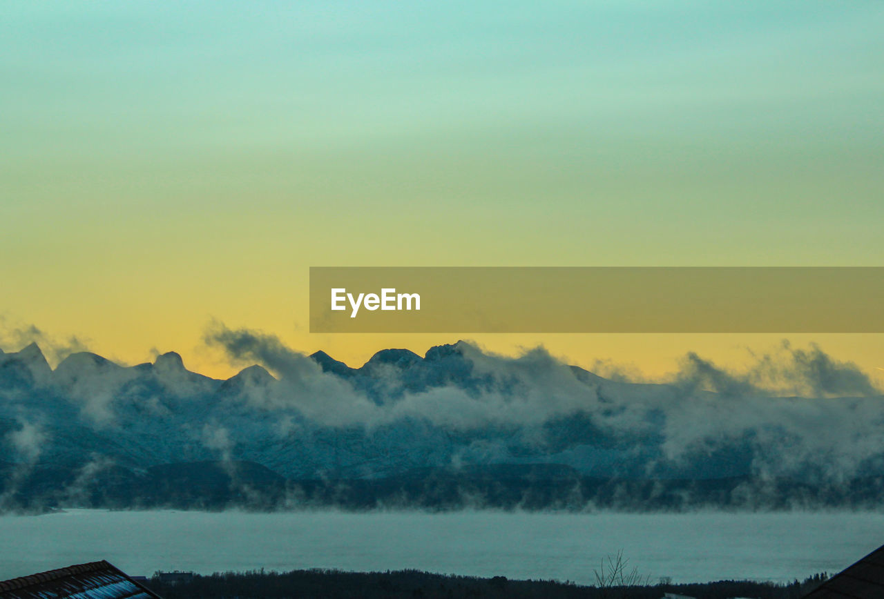 Scenic view of river by mountains against sky during sunset