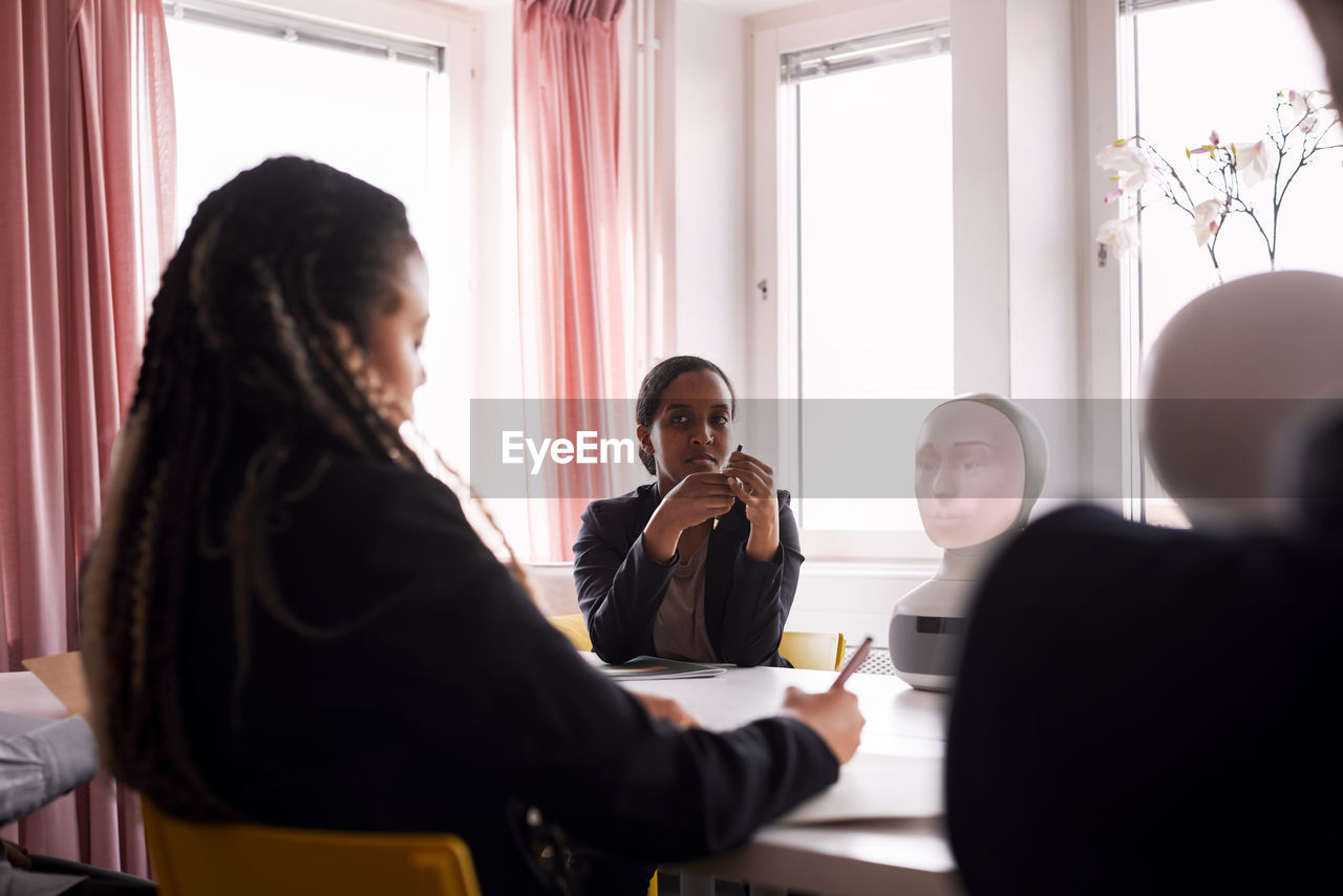 Businesswomen discussing robot voice assistant during meeting