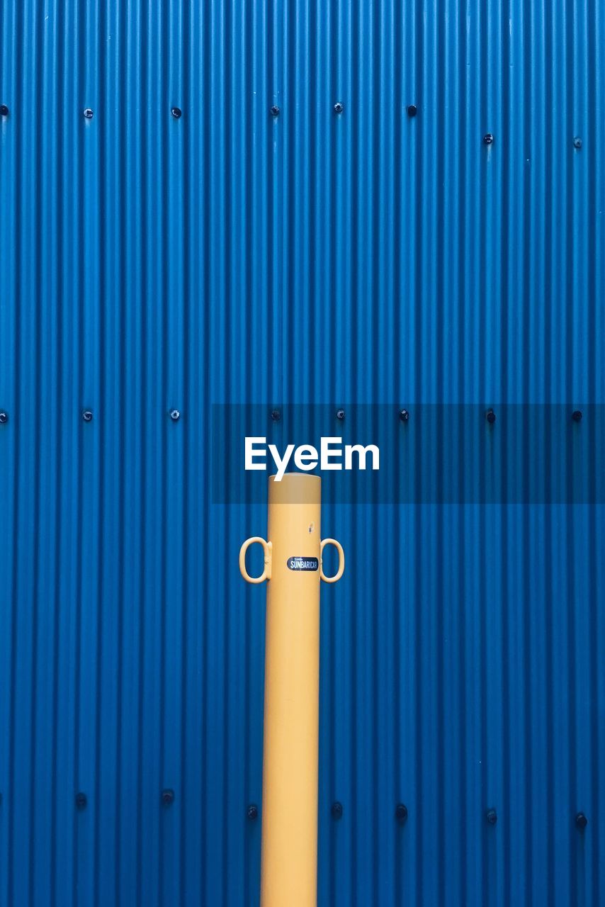 Beige pole against blue corrugated iron