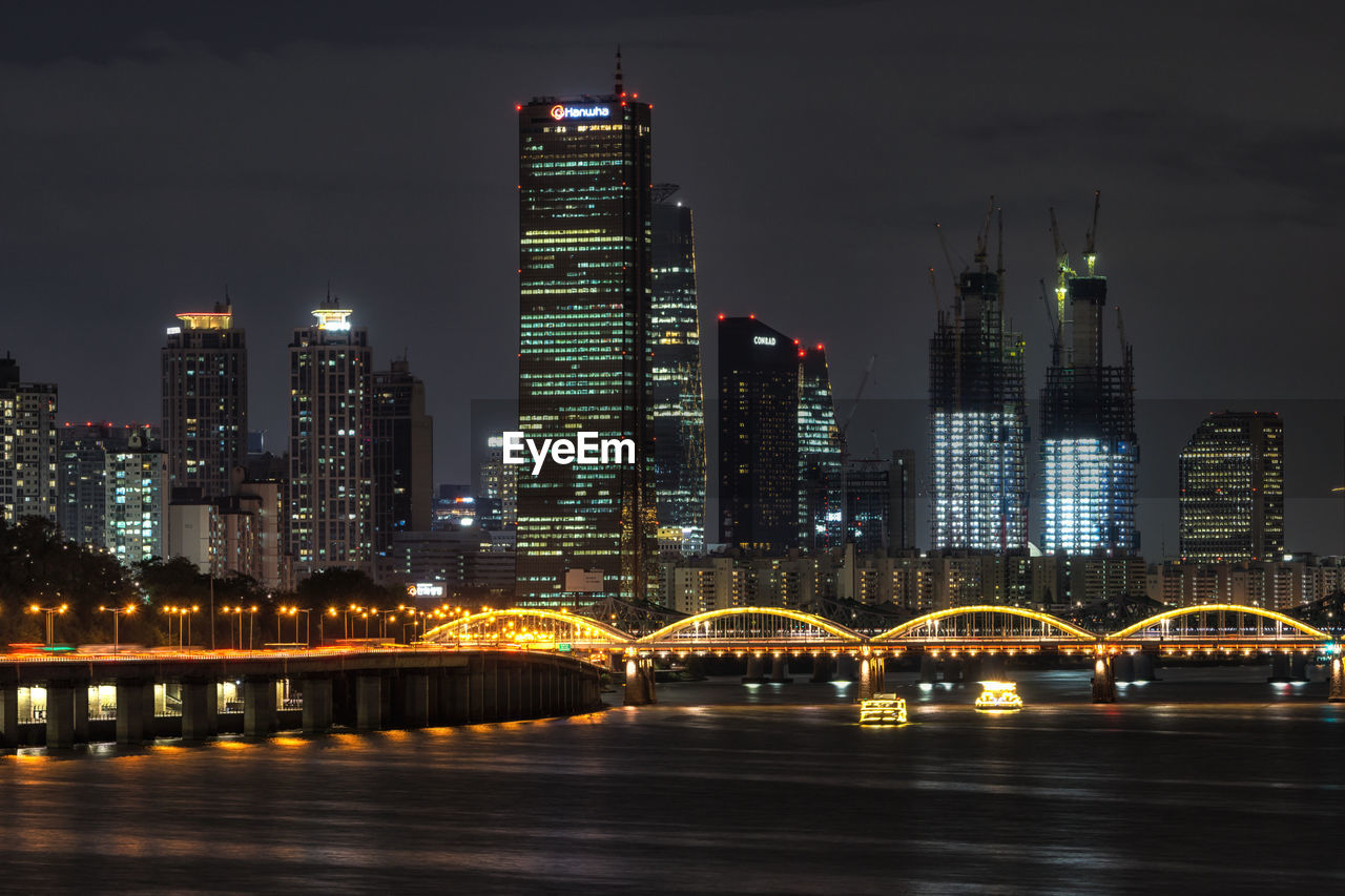 Illuminated bridge and buildings against sky at night