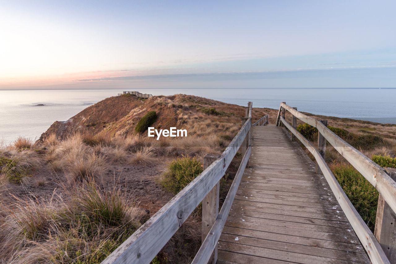 Footpath leading towards sea against sky