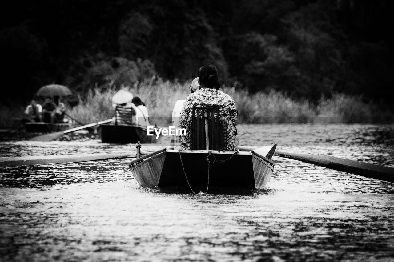 REAR VIEW OF MAN SAILING ON BOAT MOORED ON RIVER