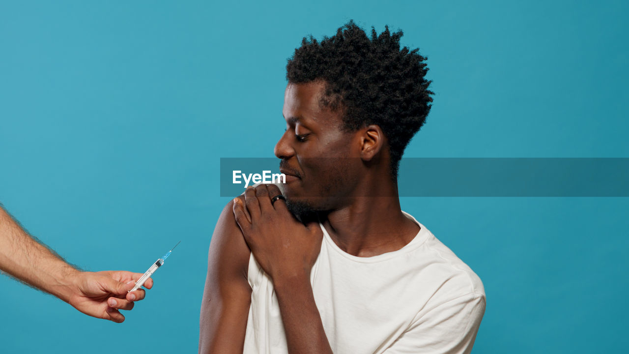 Man taking vaccine while sitting against blue background