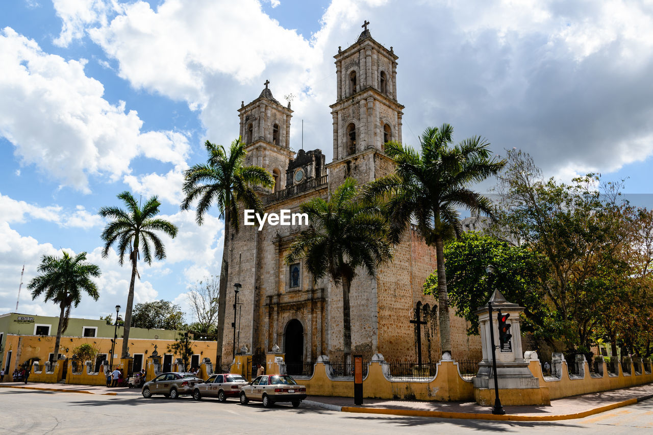 PALM TREES BY TEMPLE AGAINST SKY AND BUILDING AGAINST CLOUDY BLUE AND CATHEDRAL