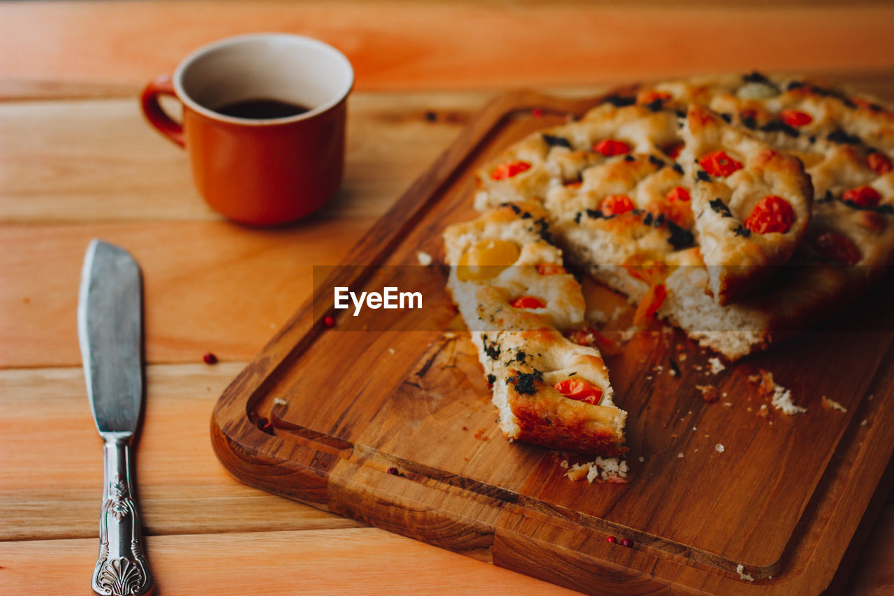 Homemade italian focaccia, with tomato and olive oil and coffee on a rustic wooden background.