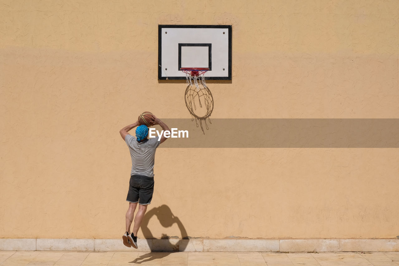 Rear view of man playing basketball against wall