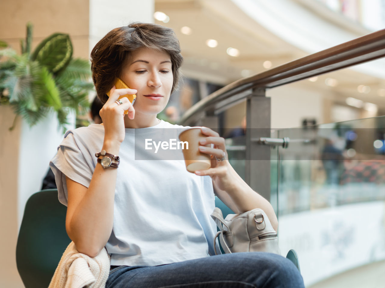 Woman is talking by smartphone and drinking coffee at shopping mall. coffee break at store.