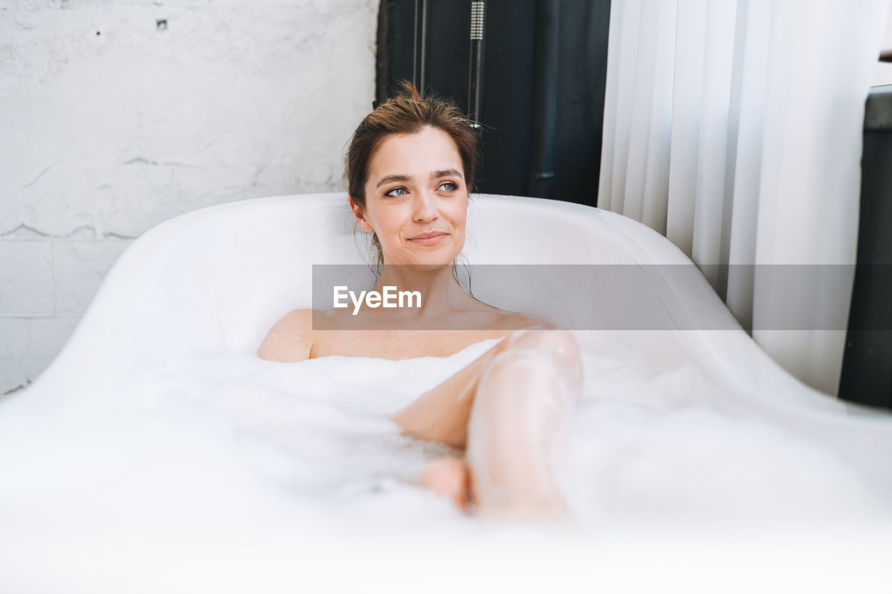 Young happy woman taking bath with foam at home, treat yourself