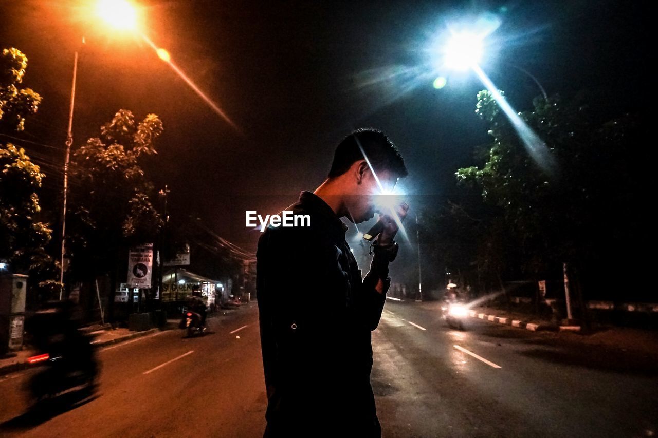 SIDE VIEW OF MAN STANDING ON ILLUMINATED STREET