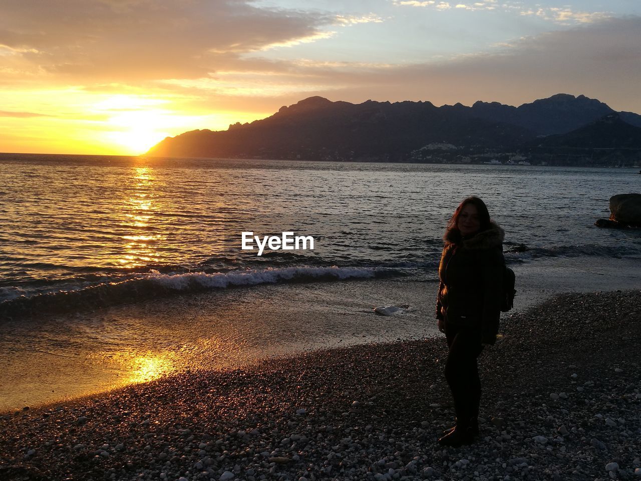 Woman standing on beach against sky during sunset