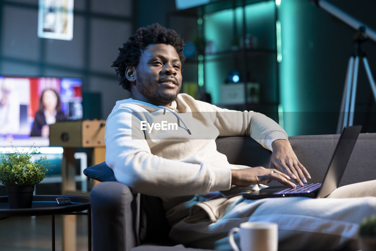 young man using laptop while sitting on sofa at home