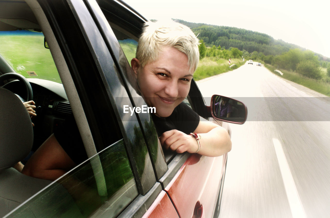 Portrait of smiling woman peeking through car window