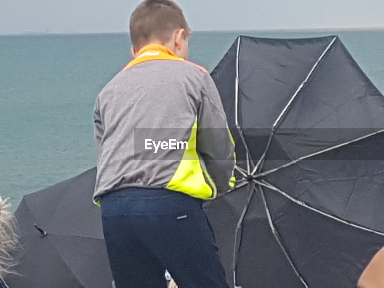 REAR VIEW OF MAN WITH UMBRELLA AT SEA