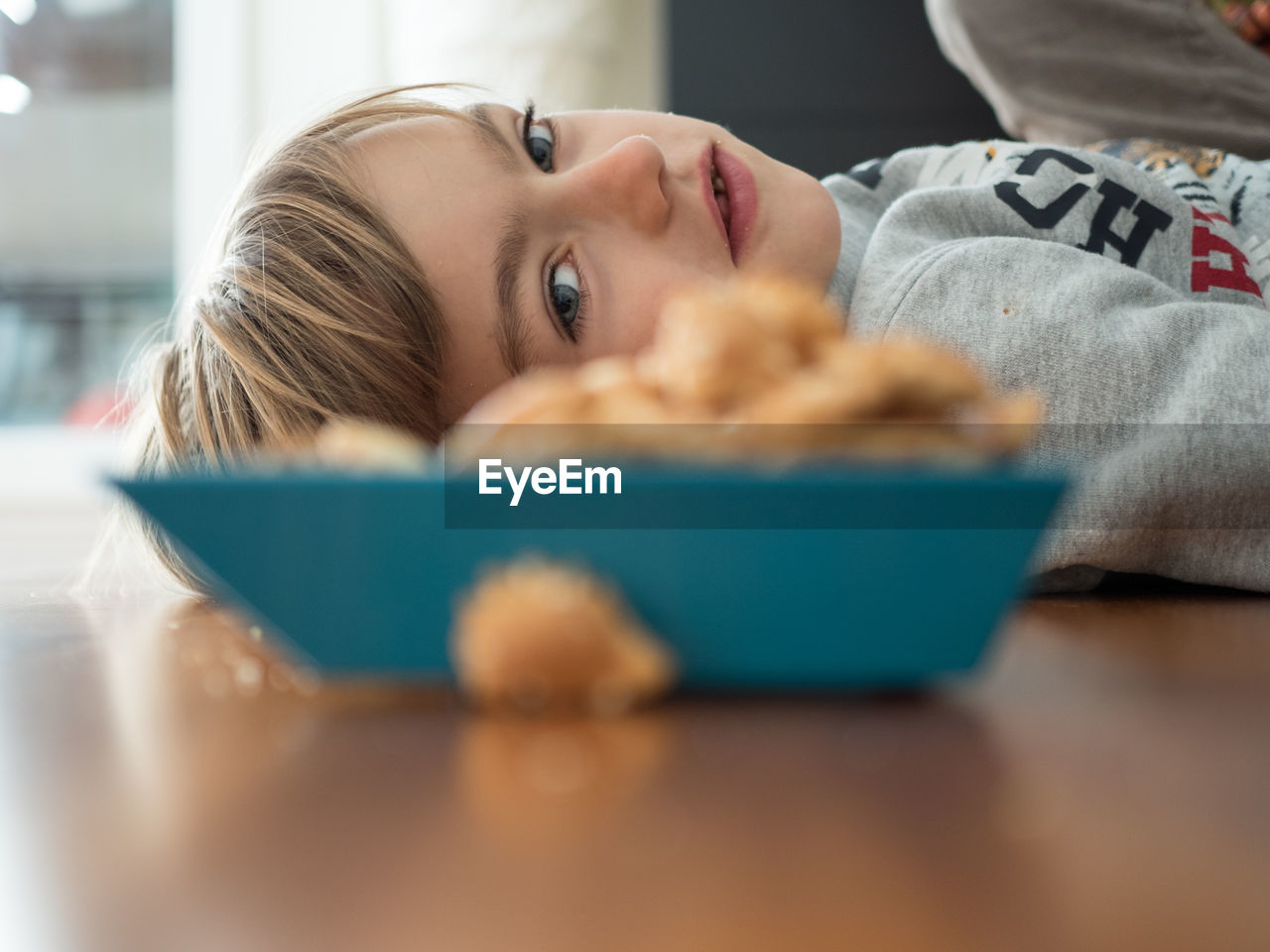 Boy lying by cereal bowl on floor at home