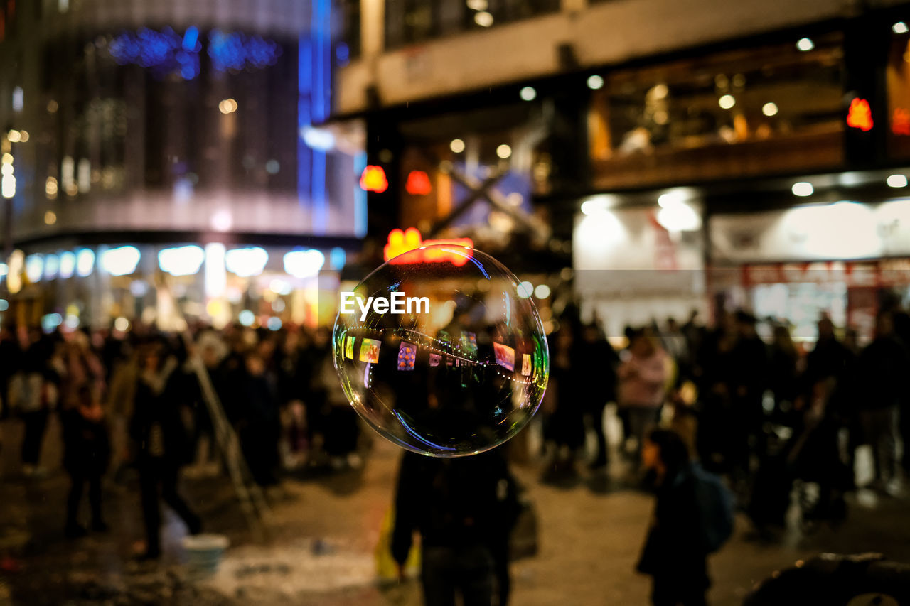 Close-up of bubble with people on illuminated street at night