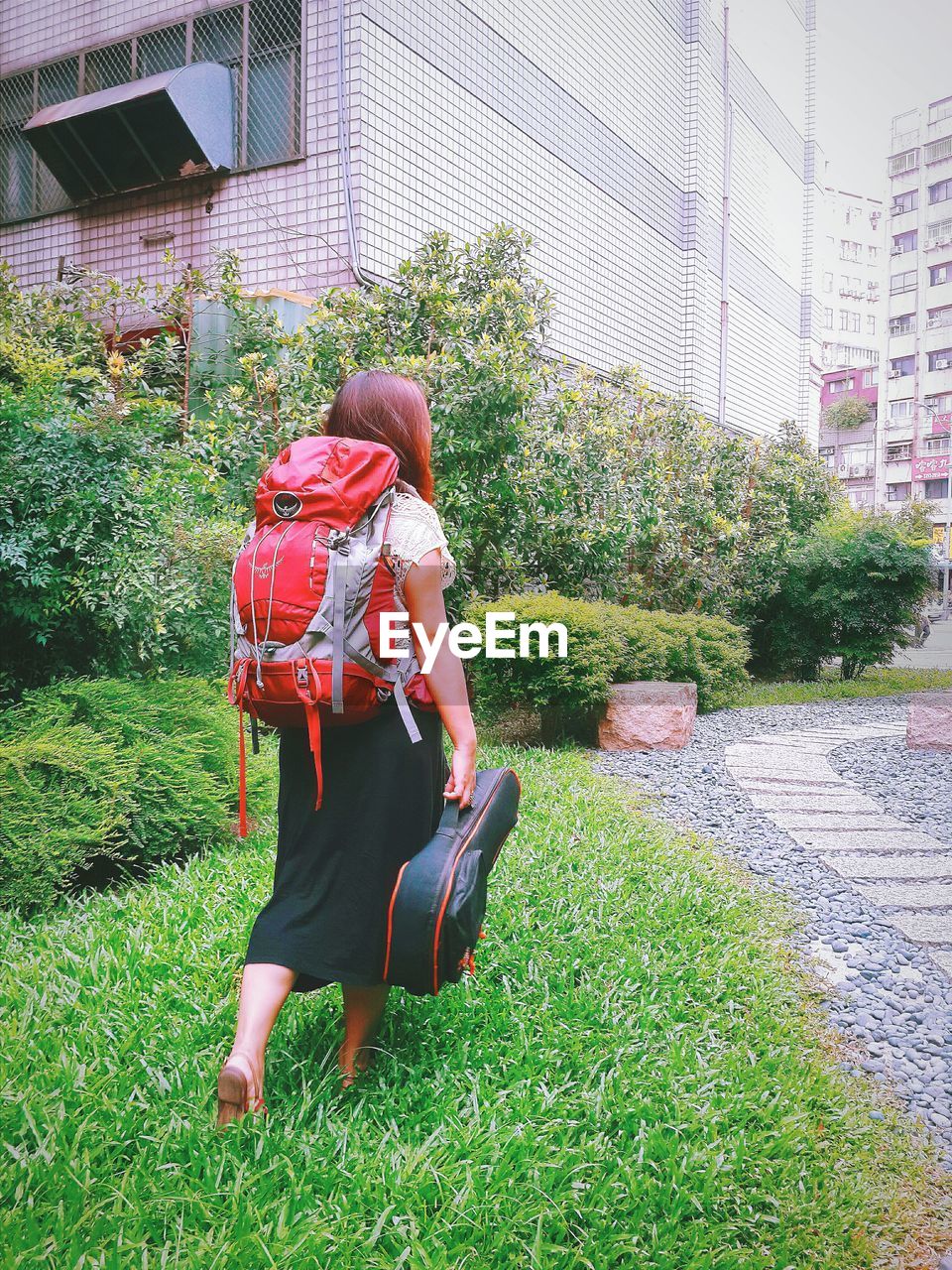 Full length rear view of backpack woman with guitar walking on grassy field