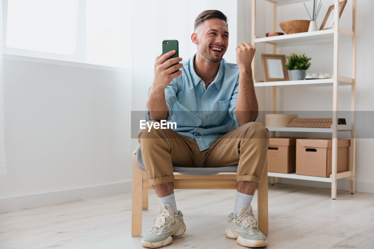 Smiling man holding mobile phone sitting at home
