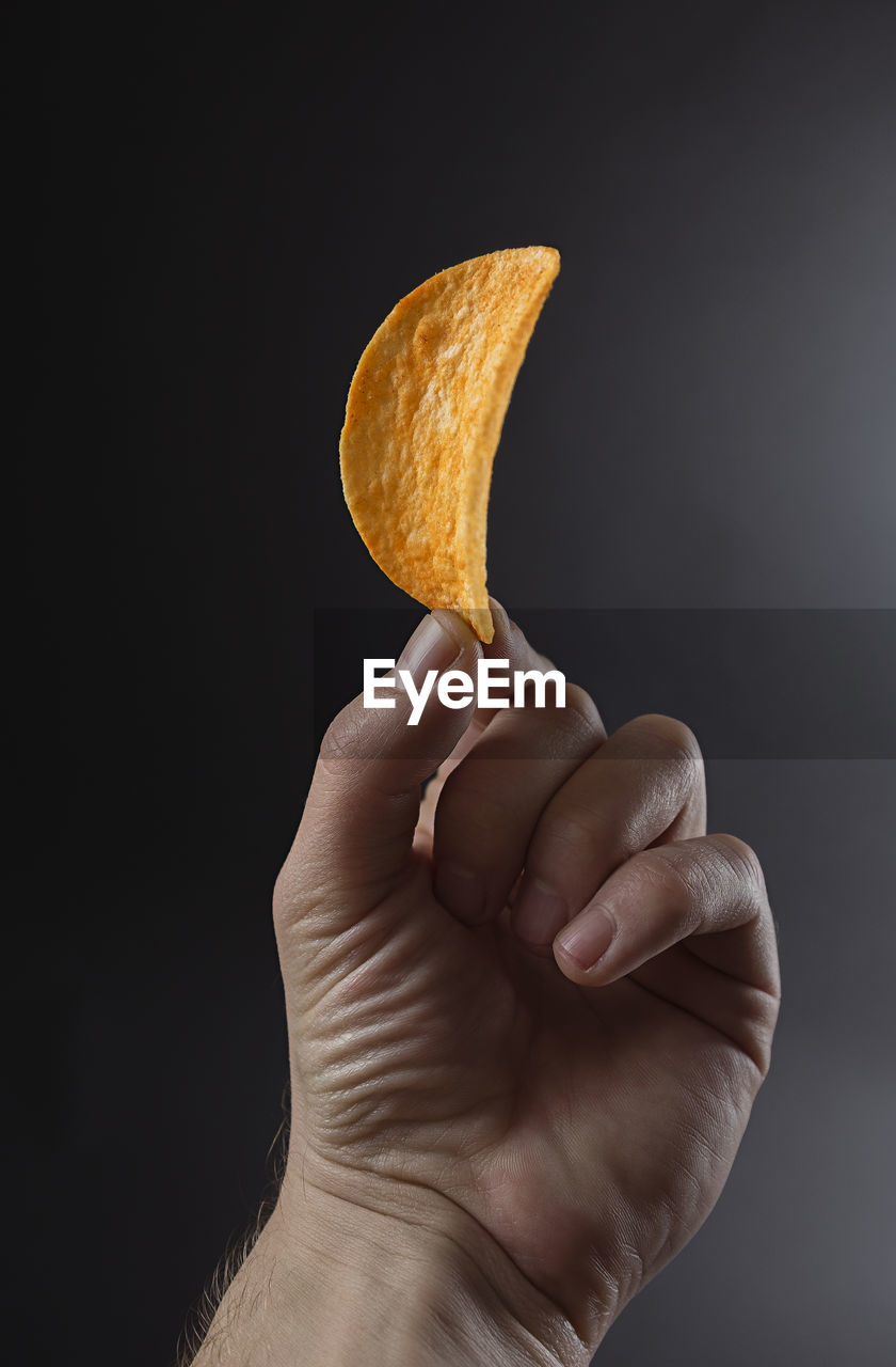 Close-up of hand holding potato chip over white background