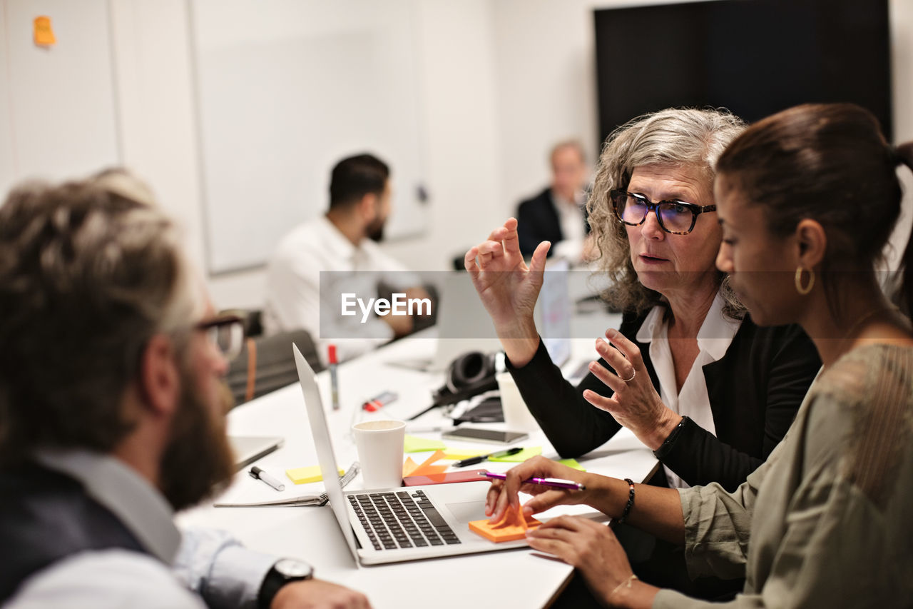 Confident mature professional discussing with colleagues in meeting at conference table