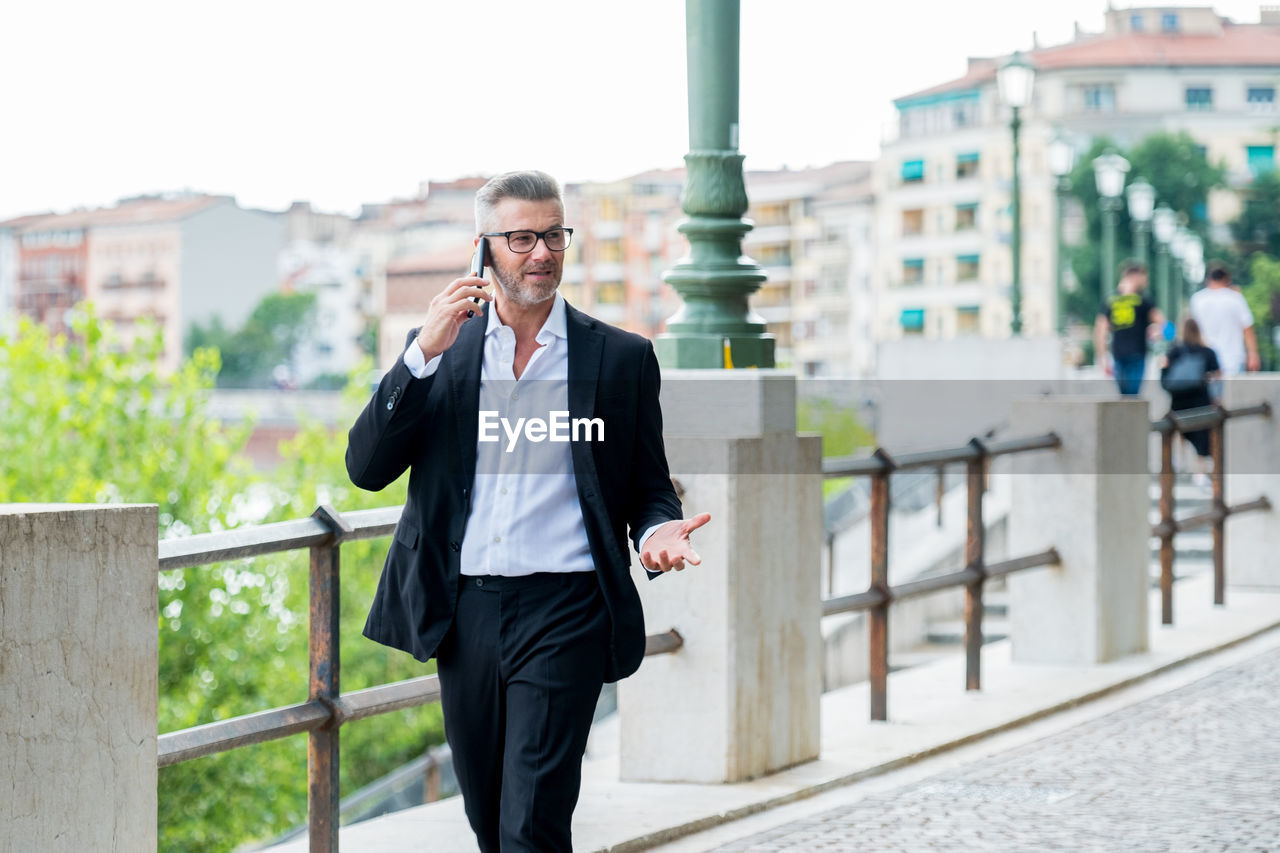 Businessman using mobile phone while walking outdoors