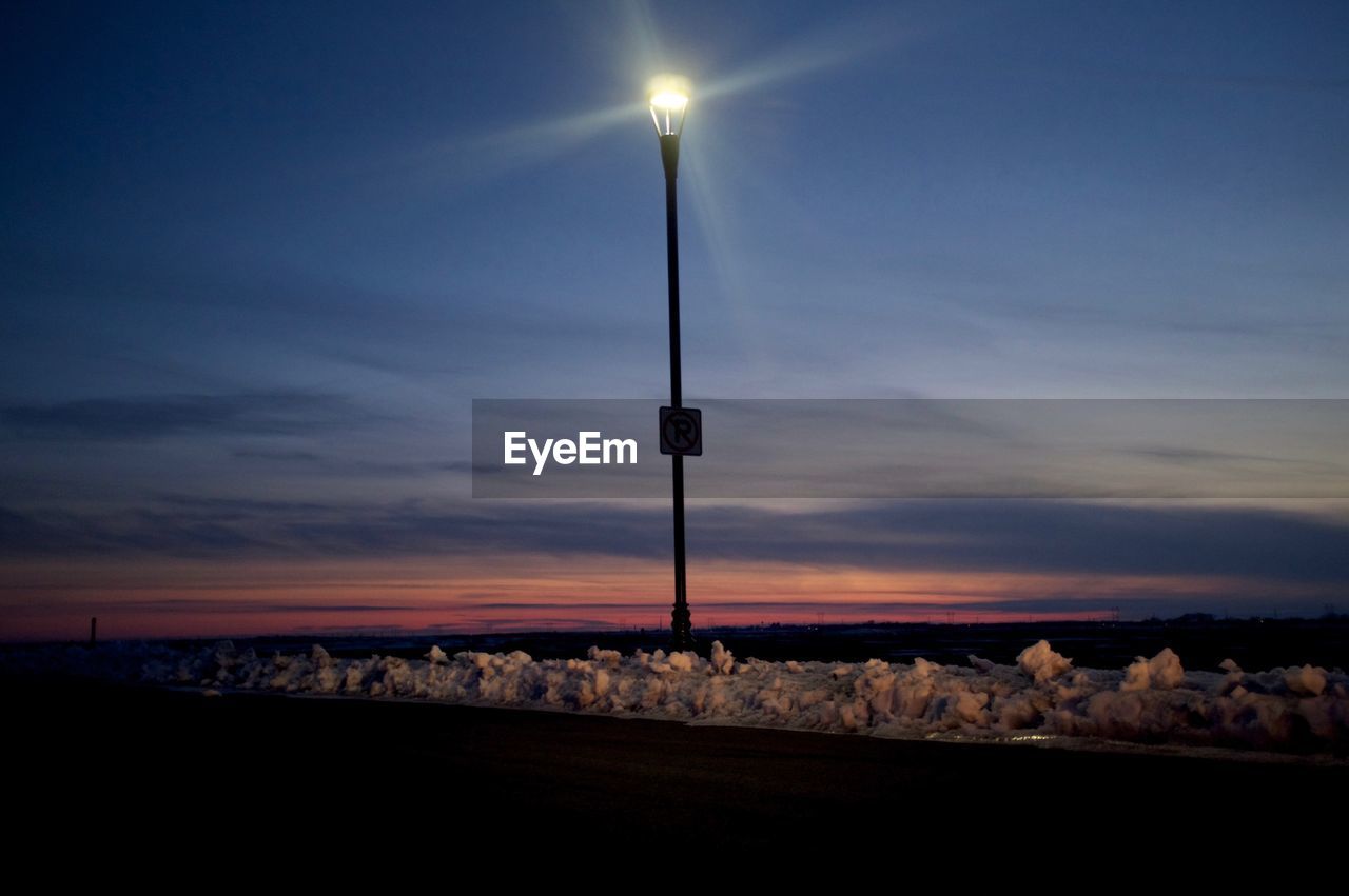 Silhouette of illuminated street light against sky at dusk