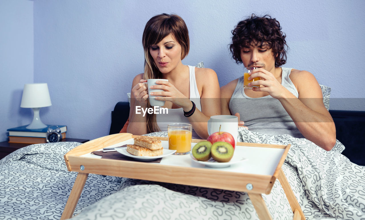 Young couple having drinks on bed at home