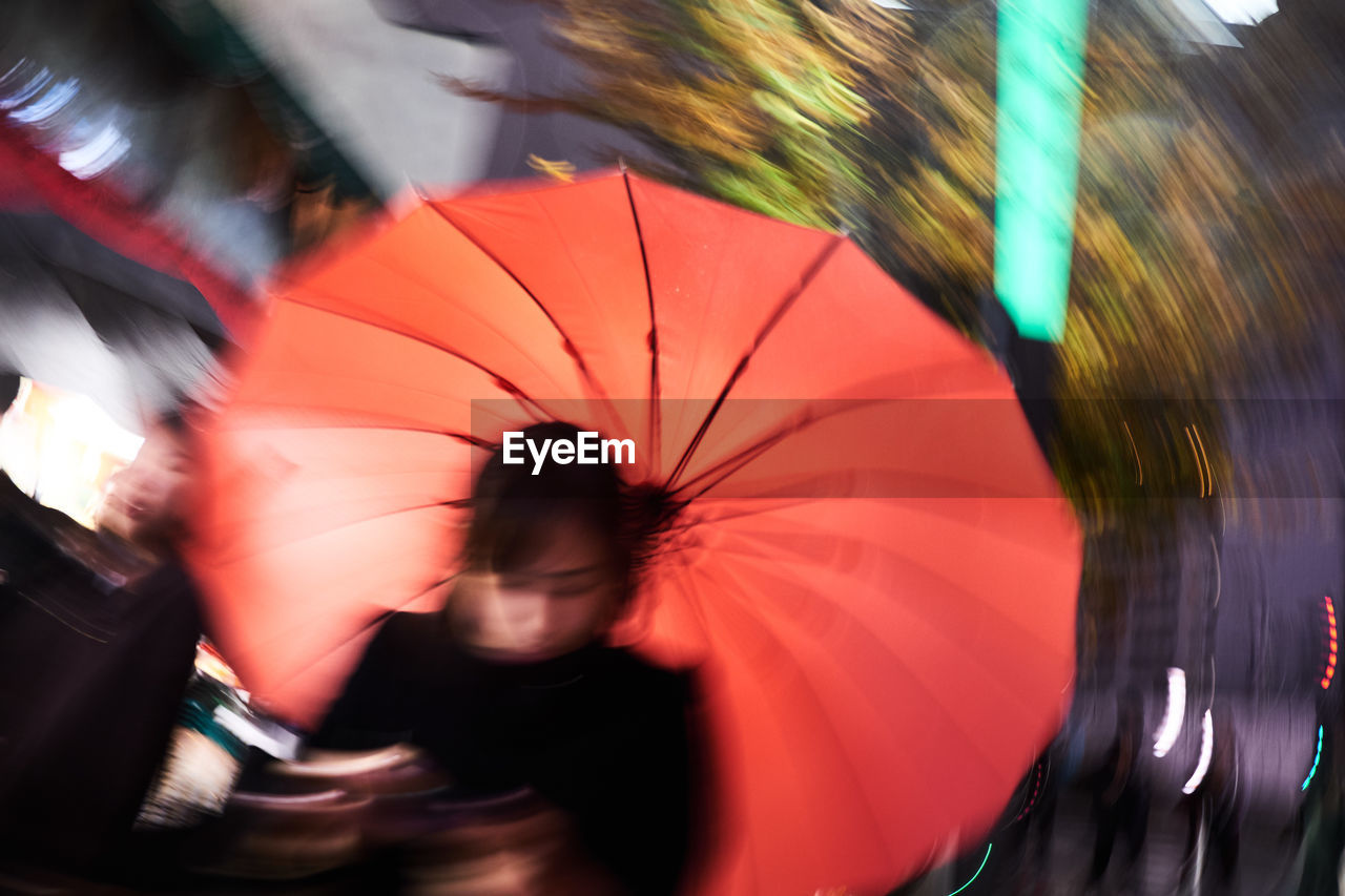 Blurred motion of woman carrying red umbrella in city during rain