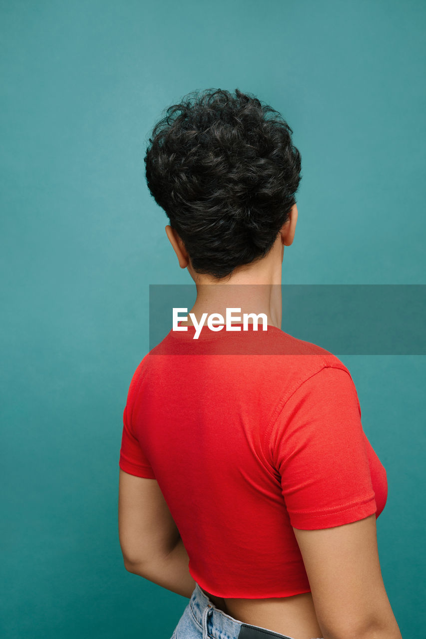 Young latina woman on her back with a red t-shirt , isolated vertical photo, tidewater green background