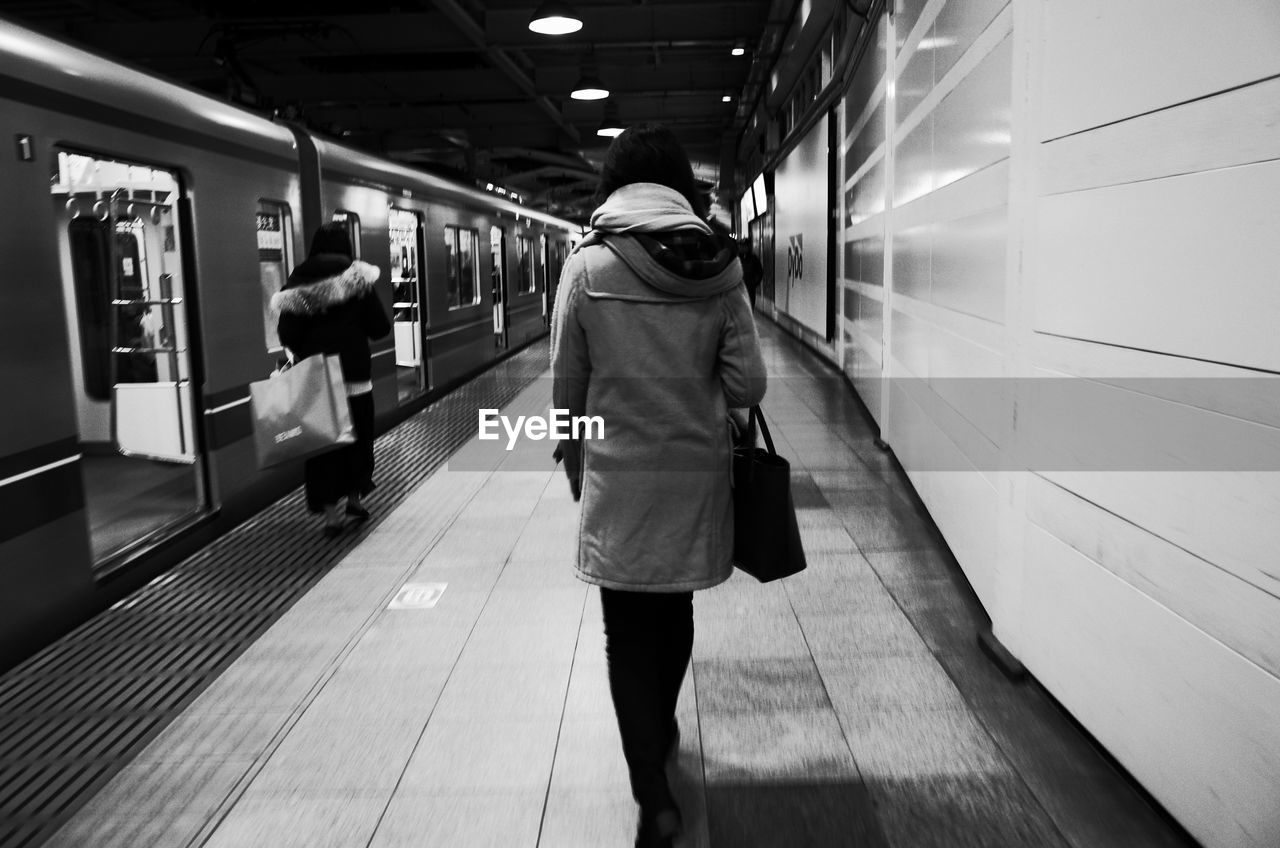 REAR VIEW OF PEOPLE WALKING ON RAILROAD STATION PLATFORM