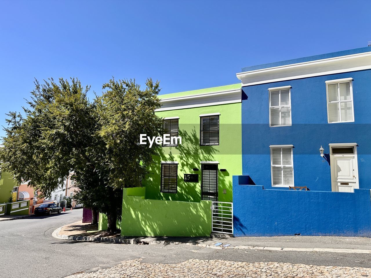 architecture, built structure, building exterior, neighbourhood, residential area, building, plant, home, blue, nature, tree, clear sky, sky, city, house, sunlight, sunny, residential district, facade, no people, day, street, outdoors, estate, transportation, window, suburb, entrance, urban area, town, road