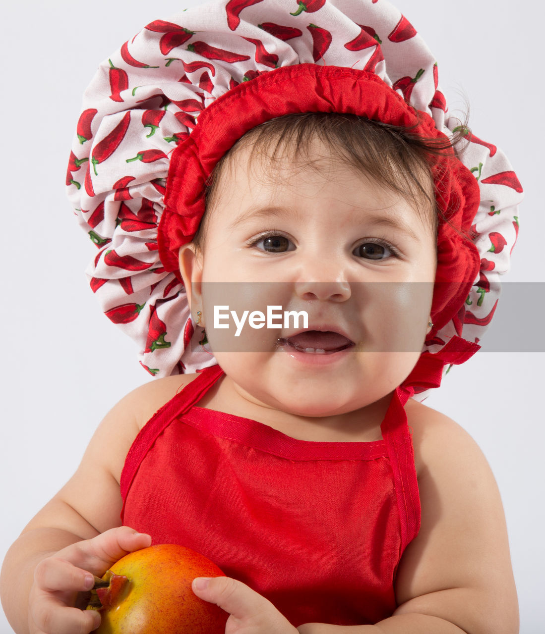 Portrait of cute baby girl holding red fruit against white background