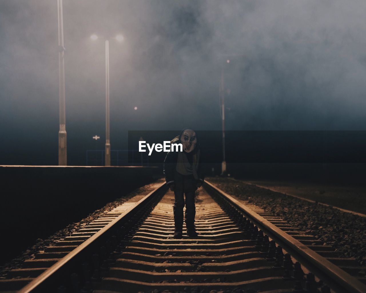 Man wearing spooky mask while standing on railroad track during halloween