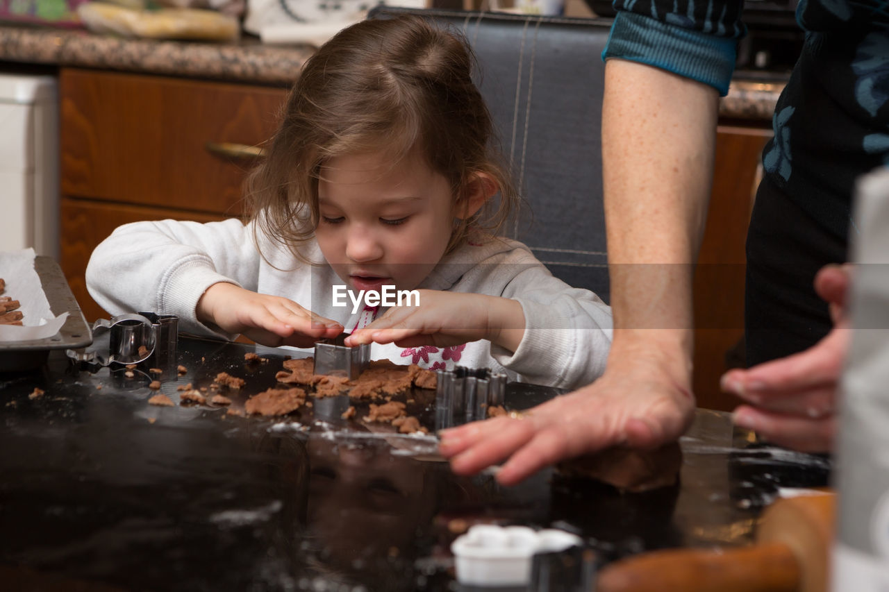 Girl preparing cookie with mother on kitchen island at home