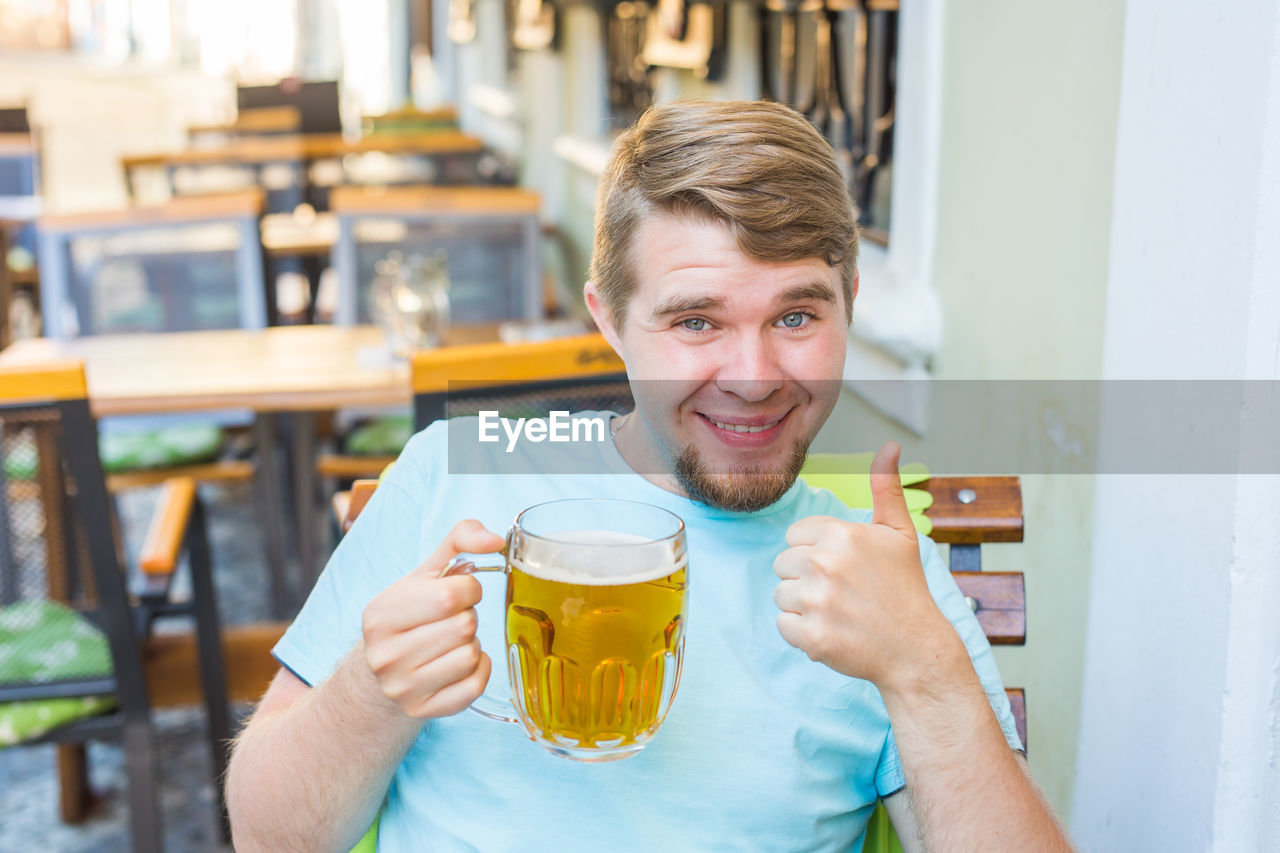 PORTRAIT OF SMILING MAN HOLDING DRINK AT RESTAURANT