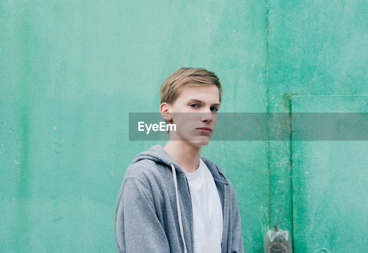 PORTRAIT OF BOY STANDING AGAINST GREEN WALL