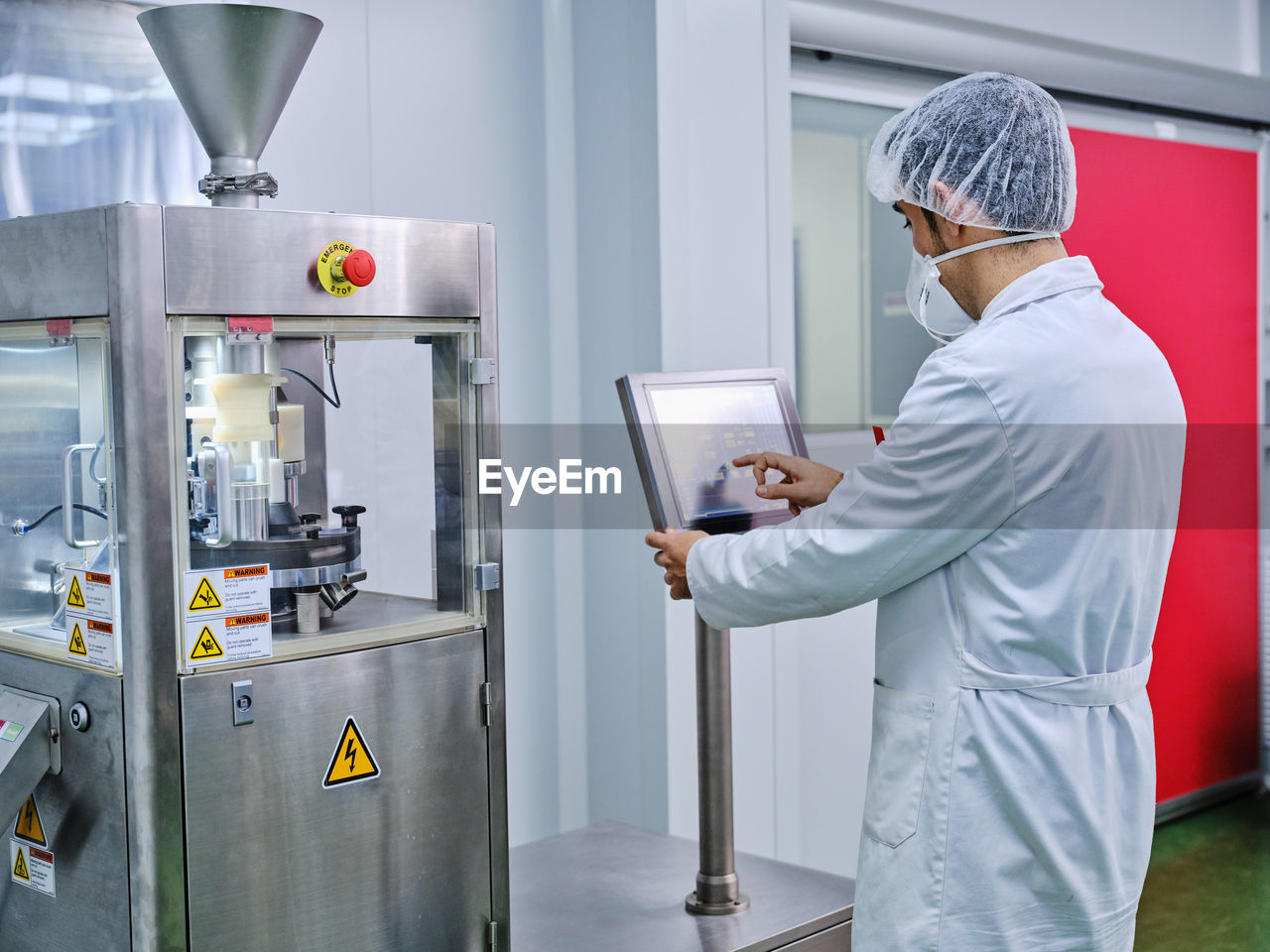 Side view of male chemist in uniform operating capsule filling machine at pharmaceutical manufacturing plant