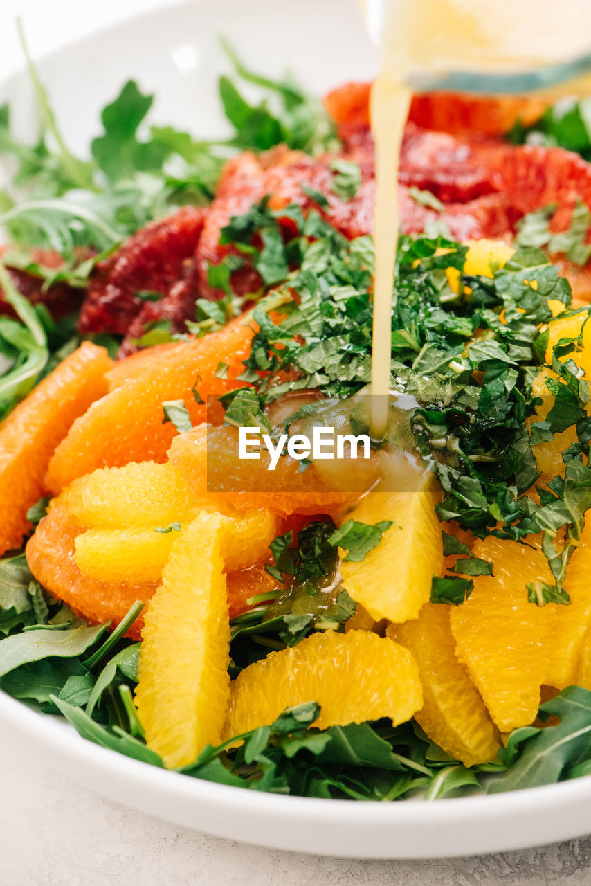 Pouring vinaigrette onto citrus arugula salad