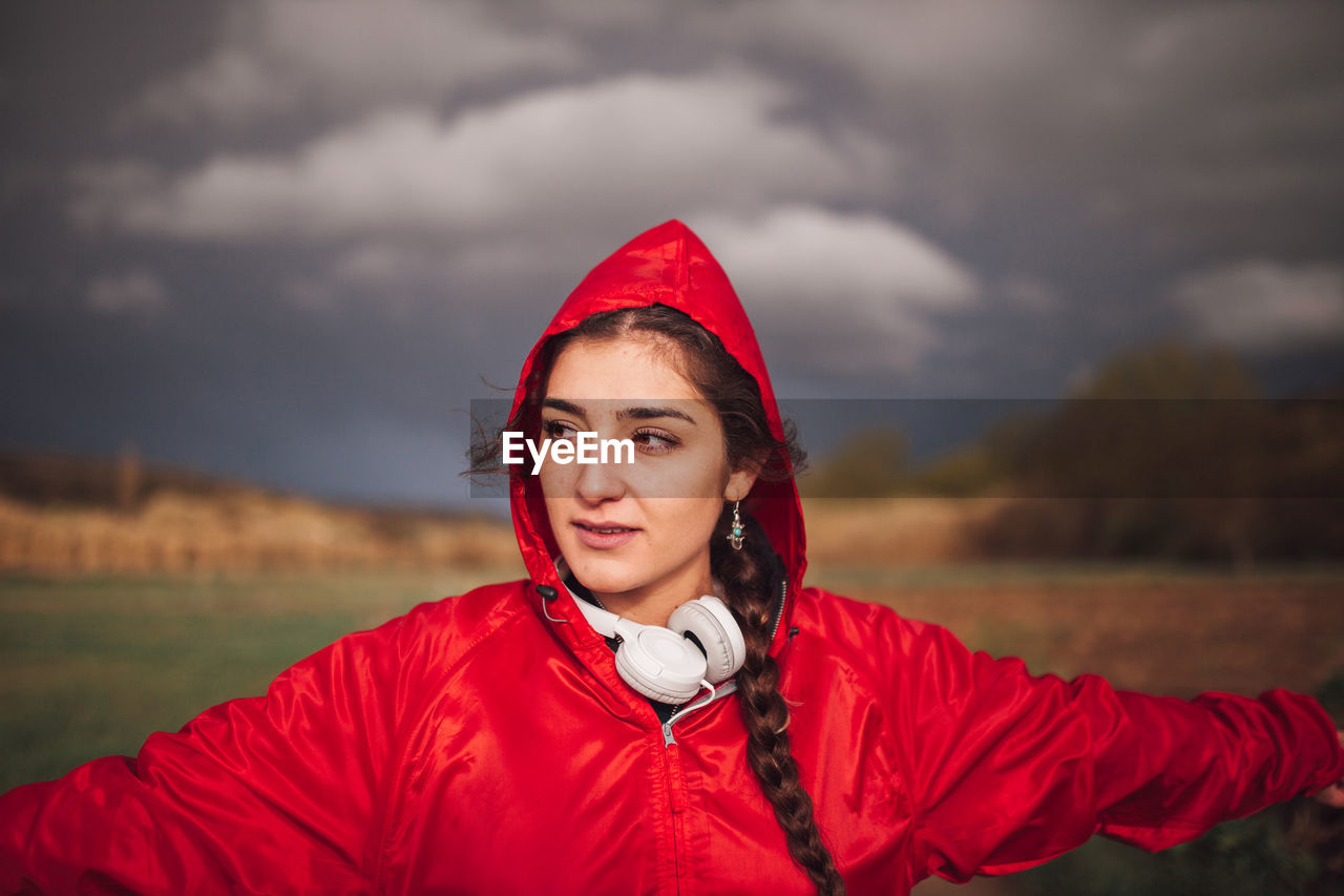 Beautiful woman standing on field against cloudy sky