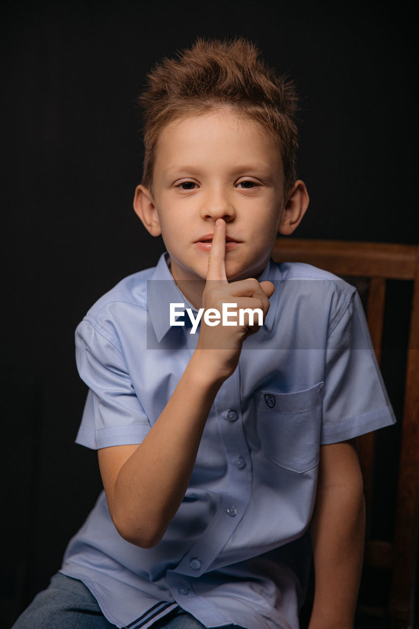 Portrait of cute boy sitting against black background