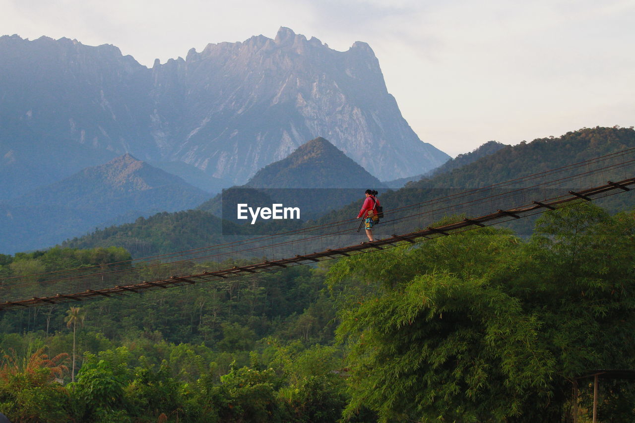 Man walking on bridge against sky