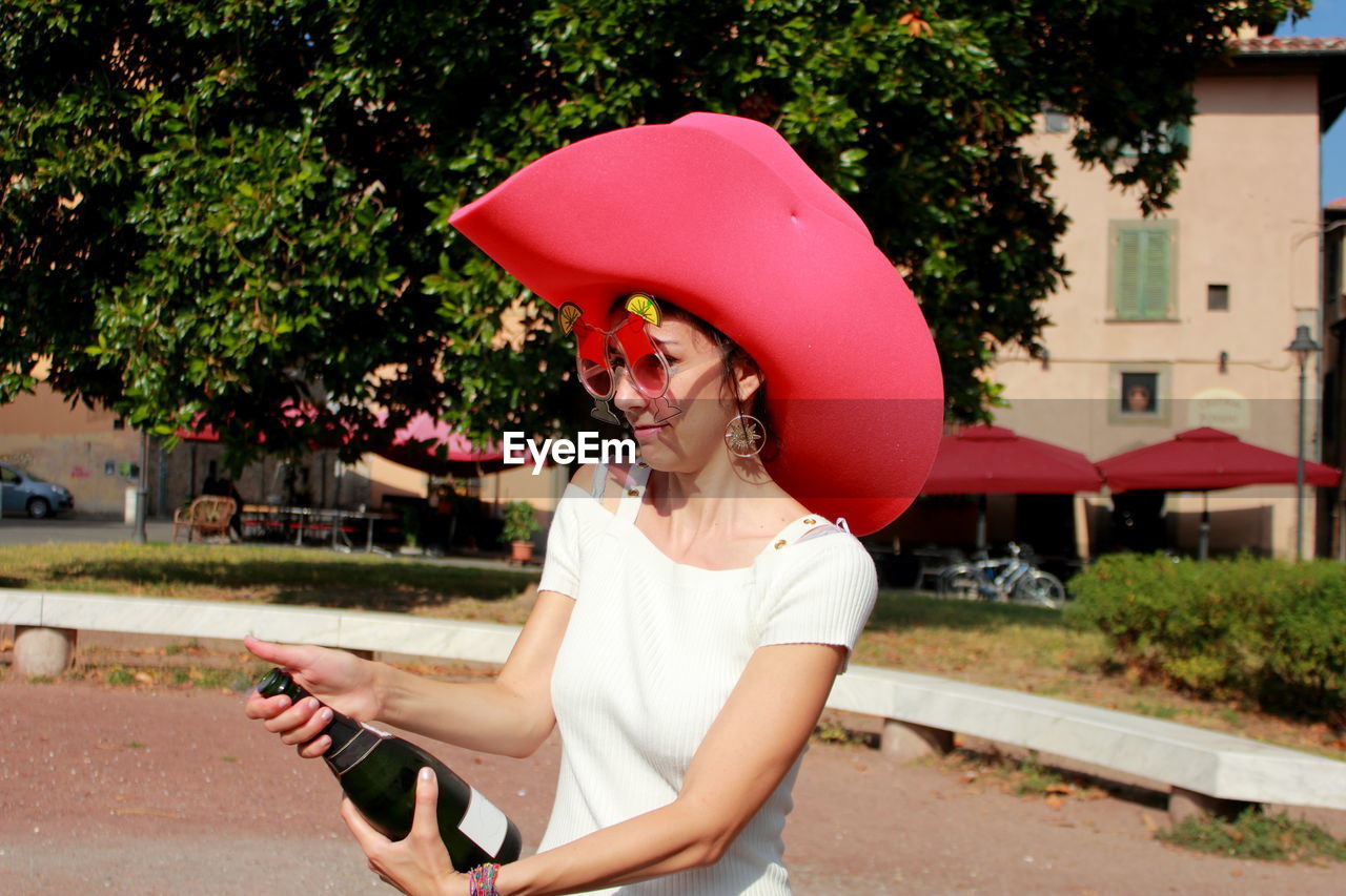 Young woman wearing pink hat while holding bottle against tree