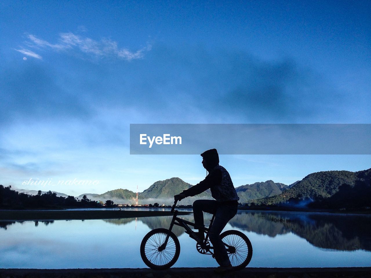 Silhouette man riding bicycle by lake against sky